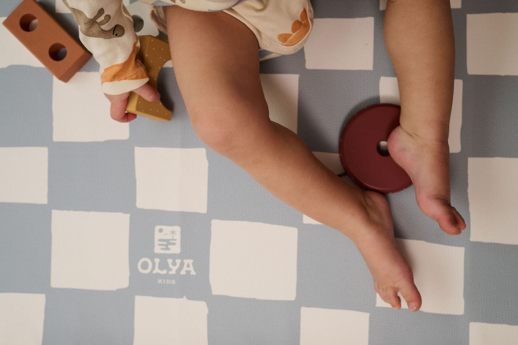 5. Child playing on blue and white checkered floor mat with OLYA KIDS logo and toy blocks