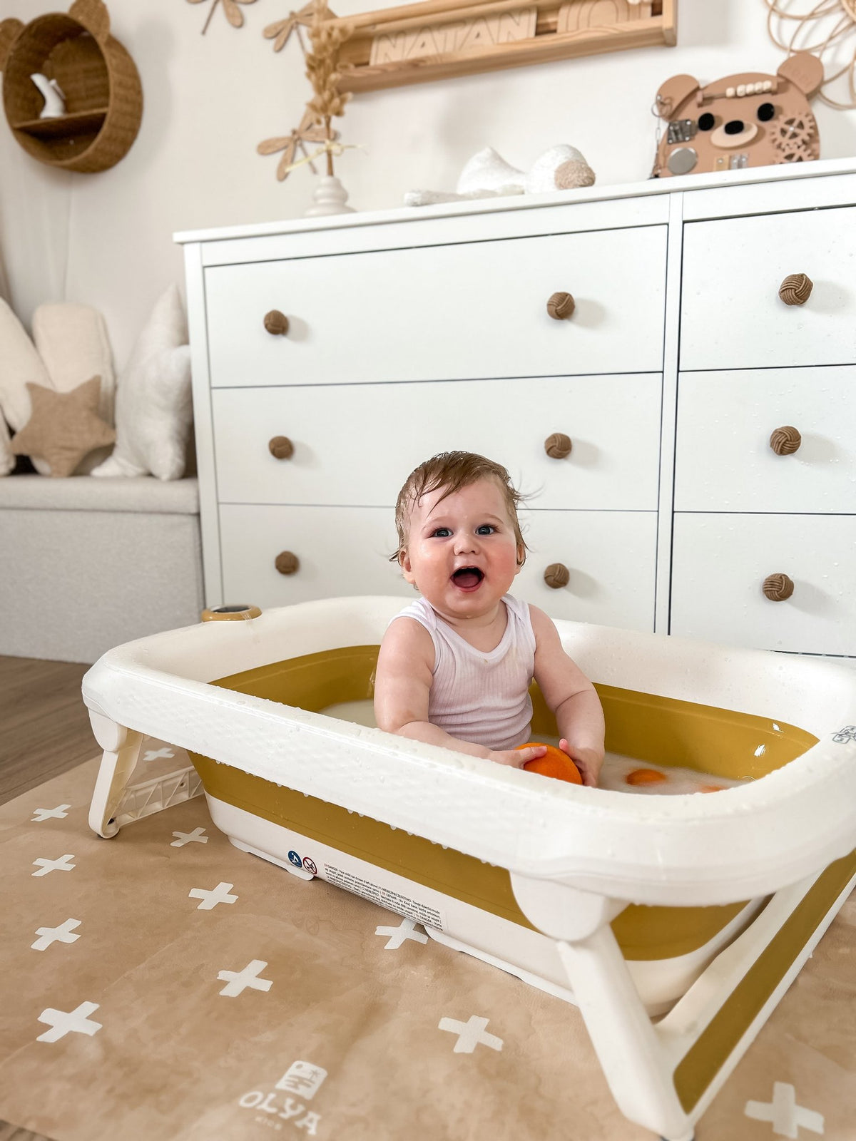 5. Happy baby in tub on beige OLYA KIDS floor mat with cross pattern, in nursery setting