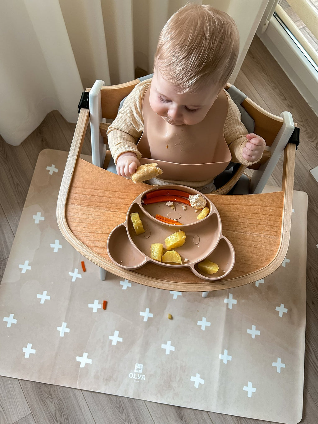 7. Baby in high chair on beige OLYA KIDS floor mat with cross pattern, enjoying meal, in bright room