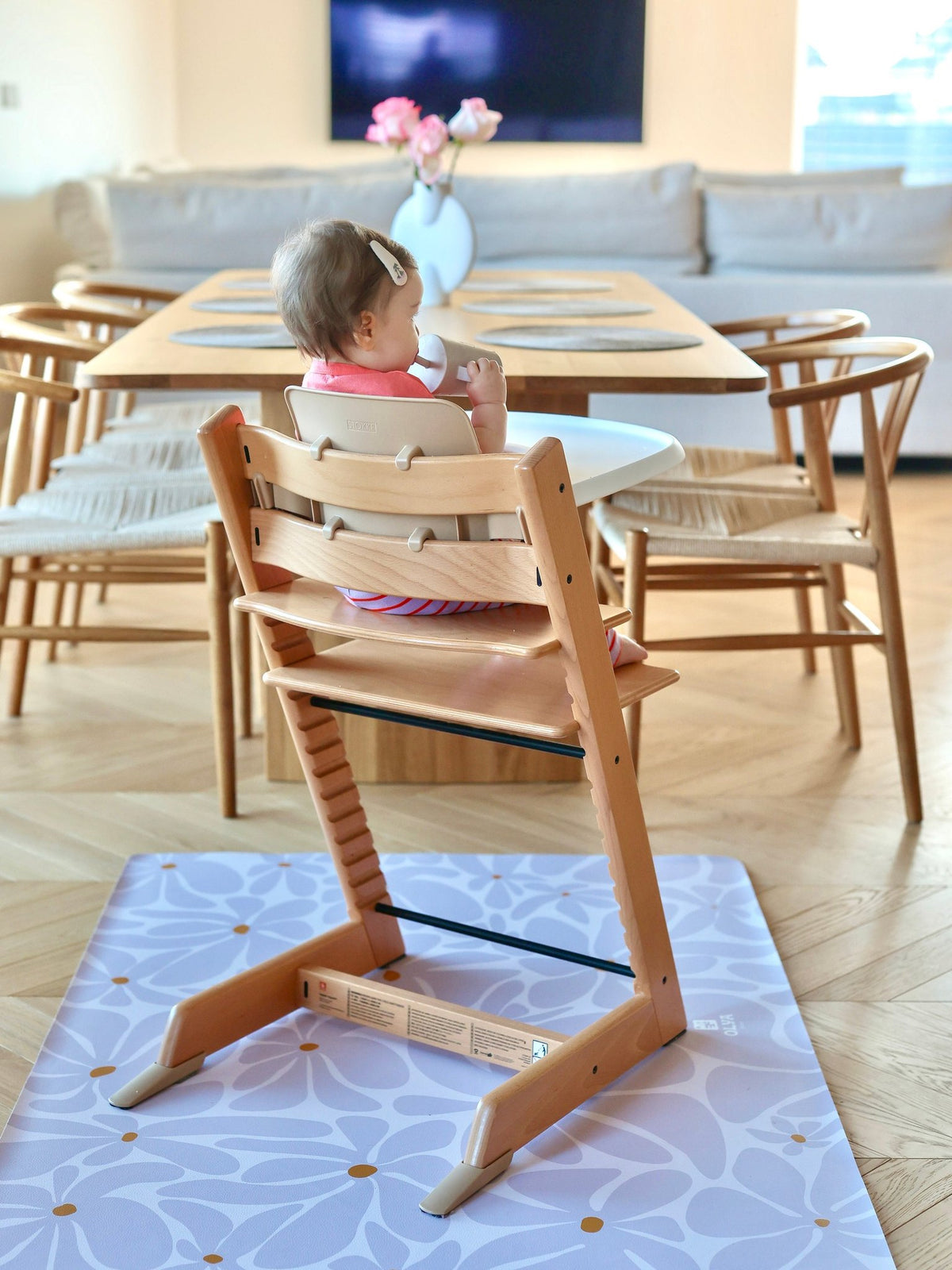 6. Back view of baby in high chair on lavender daisy-patterned floor mat