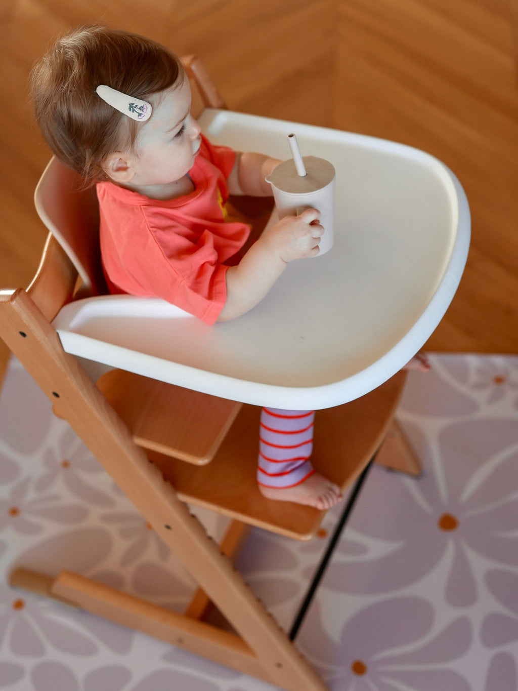 9. Baby in high chair drinking from cup on lavender daisy-patterned floor mat