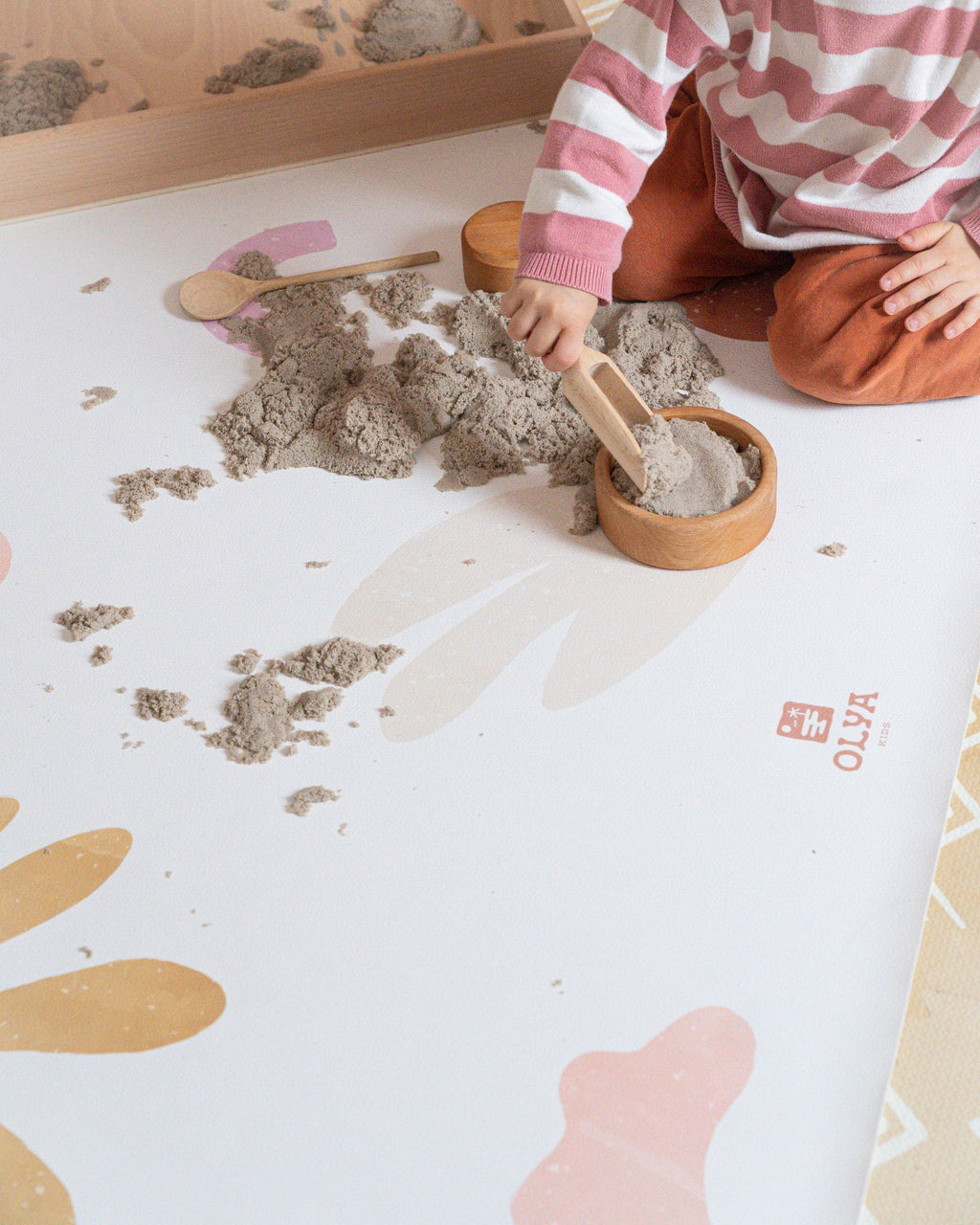 2. Child playing with sand on OLYA KIDS non-slip waterproof floor mat with abstract pastel patterns, highlighting vegan leather texture