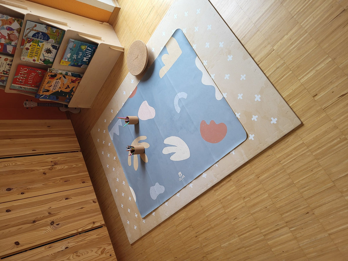 3. Kids' mealtime floor mat in organic sea design on wooden floor, surrounded by books and toys, featuring abstract shapes and OLYA KIDS logo