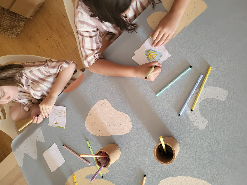 4. Two children drawing on kids' mealtime floor mat in organic sea design, featuring abstract shapes and OLYA KIDS logo
