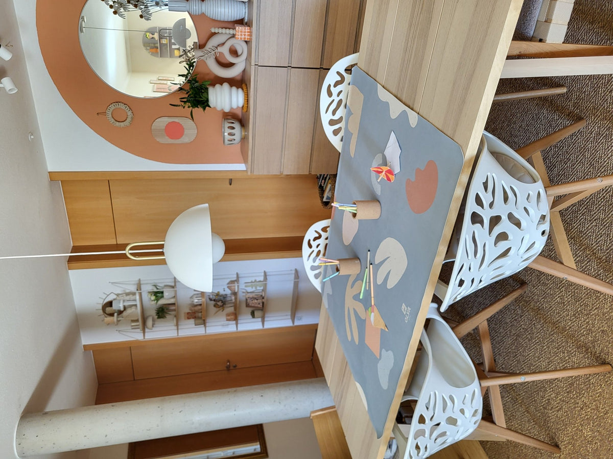 2. Kids' mealtime floor mat in organic sea design on dining table with two white chairs, featuring abstract shapes and OLYA KIDS logo