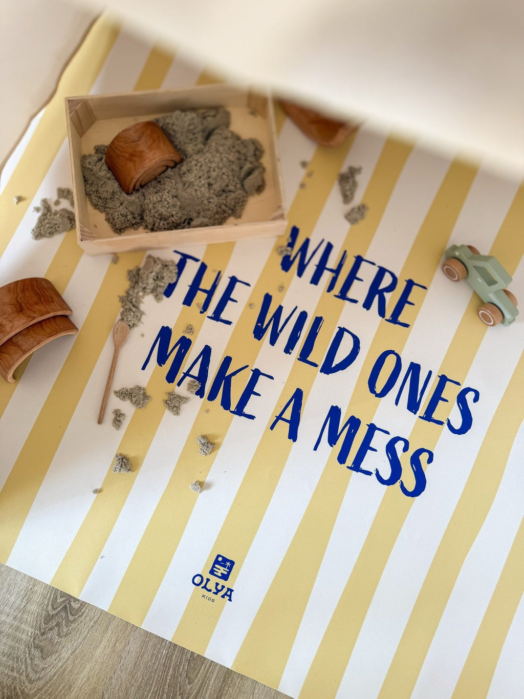 1. Yellow and white striped kids floor mat with text 'Where the wild ones make a mess' surrounded by toys and sand, OLYA KIDS logo visible