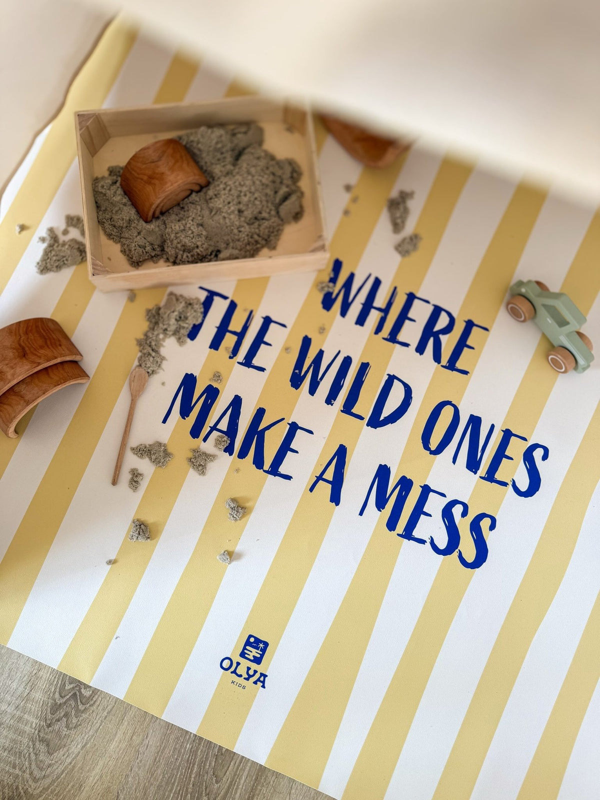 1. Yellow and white striped kids floor mat with text 'Where the wild ones make a mess' surrounded by toys and sand, OLYA KIDS logo visible
