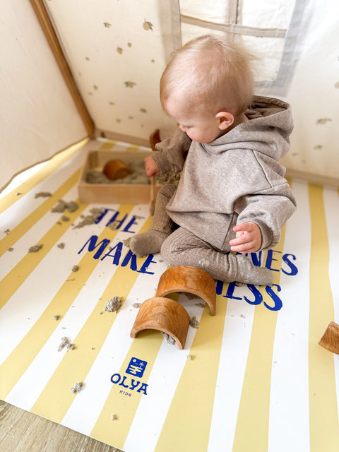 5. Baby in grey outfit playing with toys on yellow and white striped floor mat, text 'Where the wild ones make a mess' visible, OLYA KIDS logo