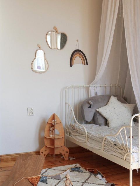 3. Apple-shaped mirror with natural plywood frame in a child's room above a bed with a canopy and wooden toys