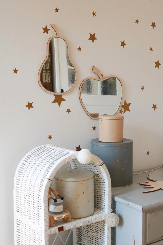 5. Apple-shaped mirror with natural plywood frame on a wall with star decals above wicker and metal storage