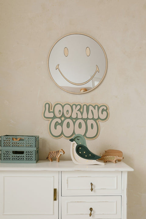 1. Emoji-shaped mirror with gold-tinted acrylic above white cabinet in kids' room, featuring 'Looking Good' sign and decorative toys