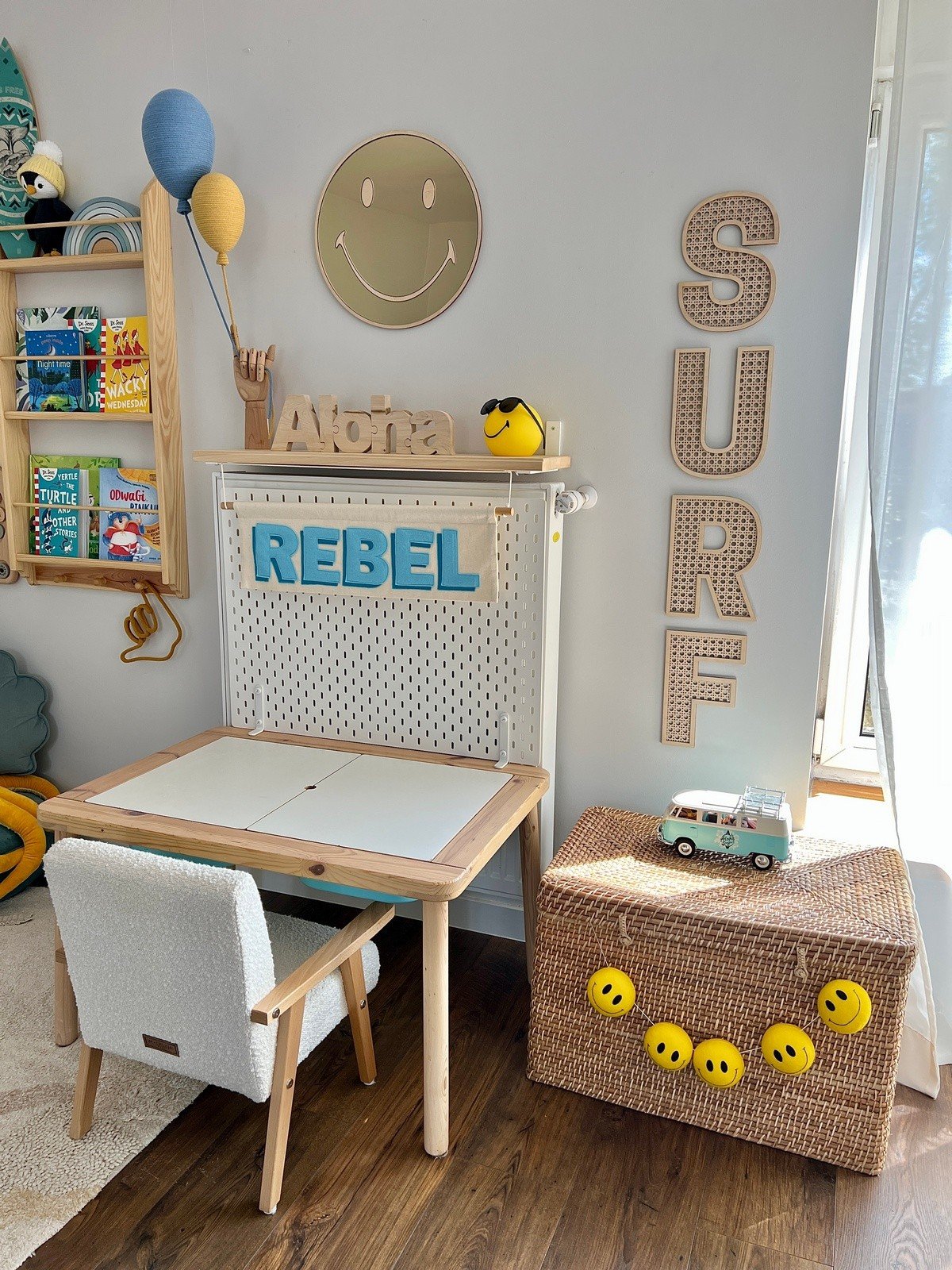 2. Emoji mirror with gold-tinted acrylic in playroom above desk, surrounded by 'Rebel' and 'Surf' decor, with toys and books
