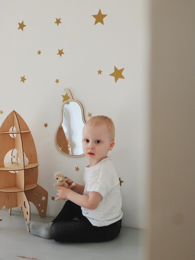 4. Child sitting near pear-shaped mirror with plywood frame, gold star decals, and wooden rocket decor.