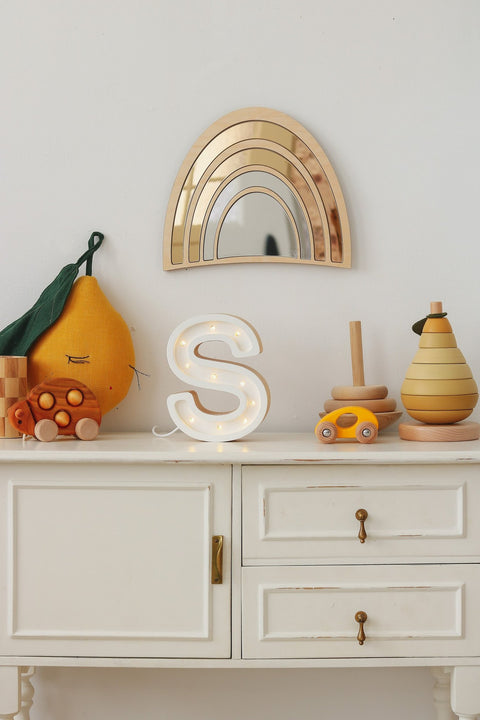3. Gold-tinted rainbow mirror with plywood frame on nursery shelf with toys and decorative letter S