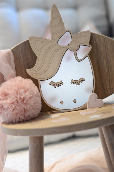 3. Close-up of unicorn-shaped mirror with natural plywood frame on wooden chair, pink pom-pom and heart decor