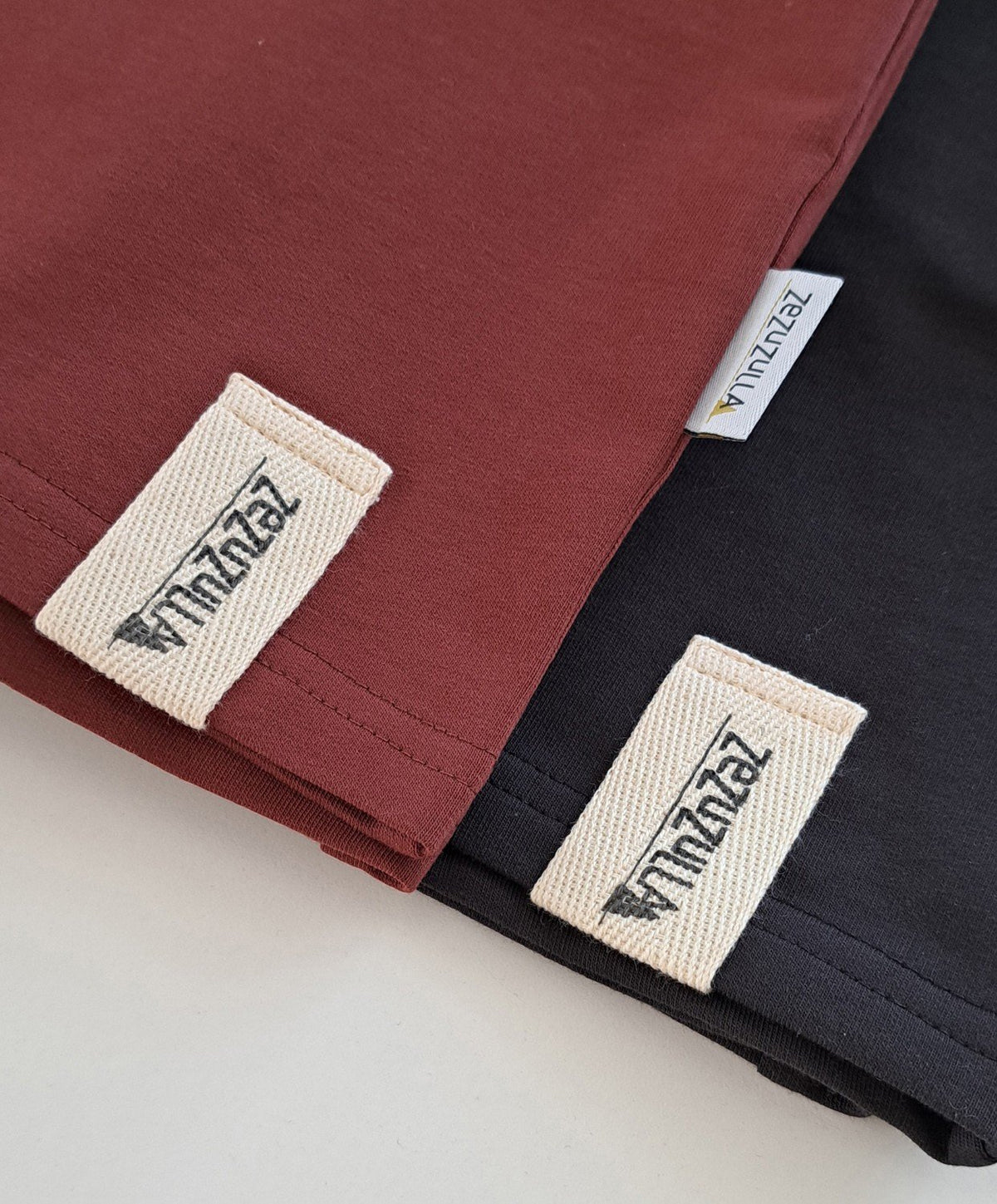 2. Close-up of Zezuzulla logo tags on rust and black cotton shorts, highlighting fabric texture