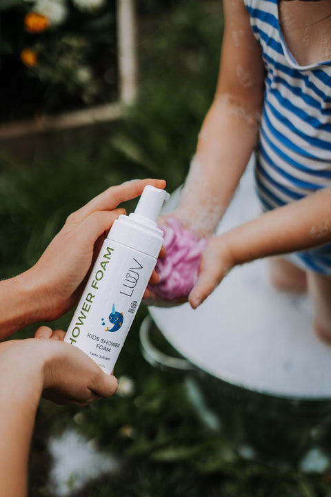 1. Child in blue striped swimsuit playing with LUUV Kid's Shower Foam Pear COSMOS in outdoor setting