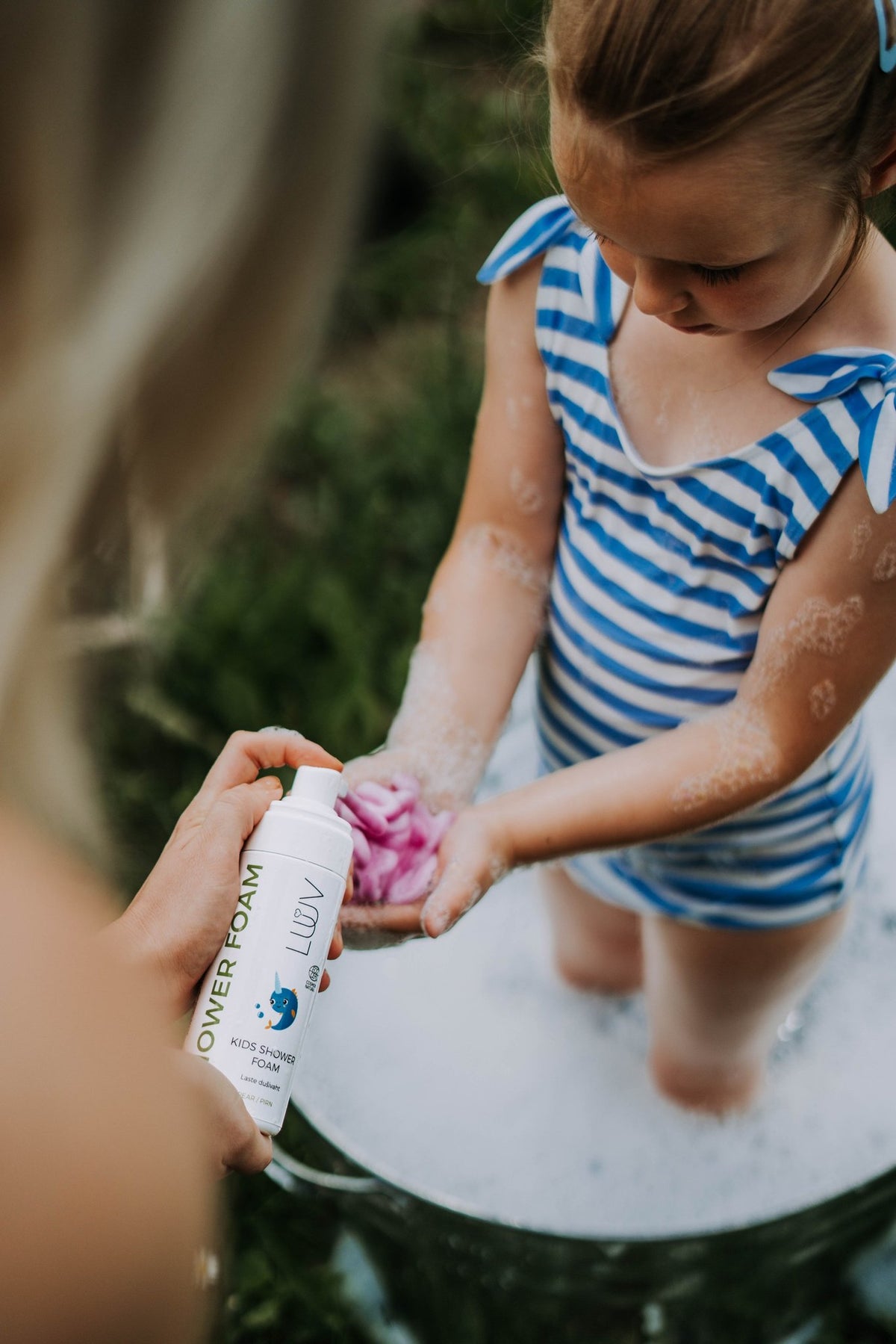 5. Girl in blue striped swimsuit receiving LUUV Kid's Shower Foam Pear COSMOS from adult in outdoor setting