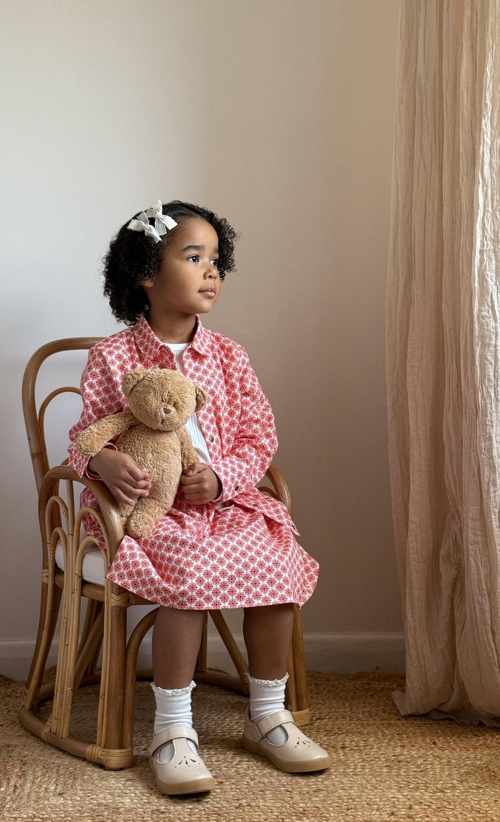 1. Young girl sitting on chair wearing Zezuzulla red and white skirt and jacket, holding teddy bear