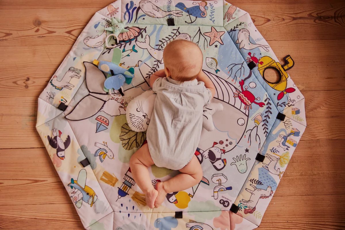 7. Baby lying on Kinderkraft Smartplay Sea playmat with colorful underwater theme