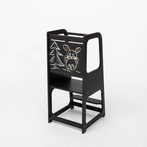 1. Black Montessori kitchen helper tower with blackboard panel featuring a drawing of a rabbit and tree, shown in a studio setting