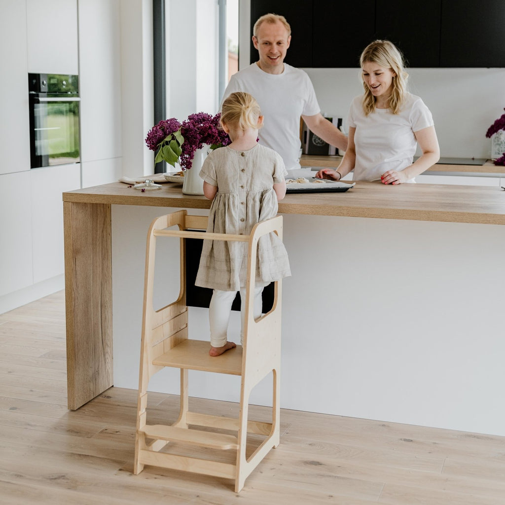 1. Family with child using natural wood Montessori kitchen helper tower in bright kitchen
