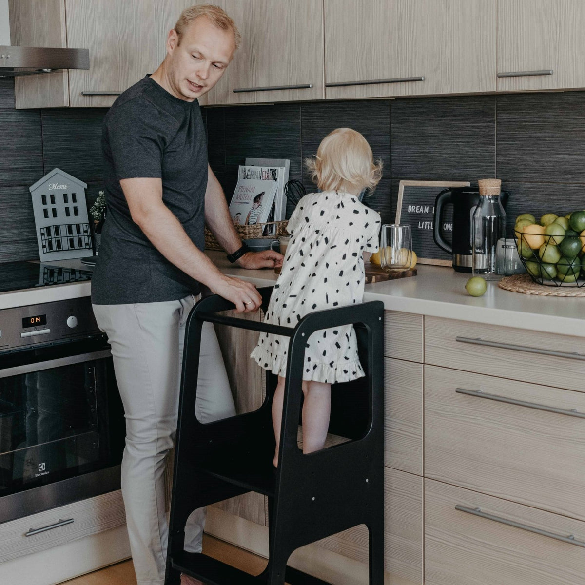 2. Man and child using black Montessori kitchen helper tower in modern kitchen setting