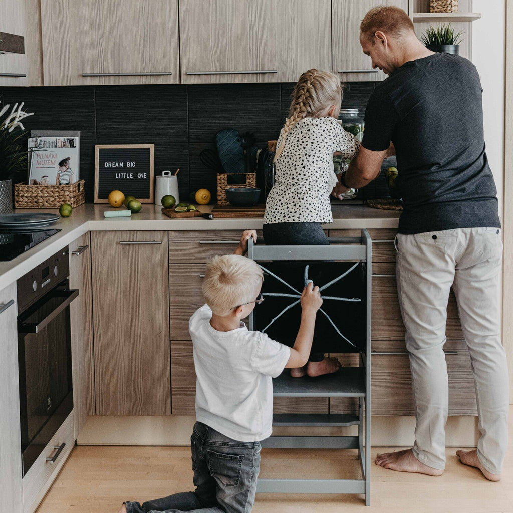 1. Family with children using grey Montessori kitchen helper tower in kitchen, child drawing on blackboard