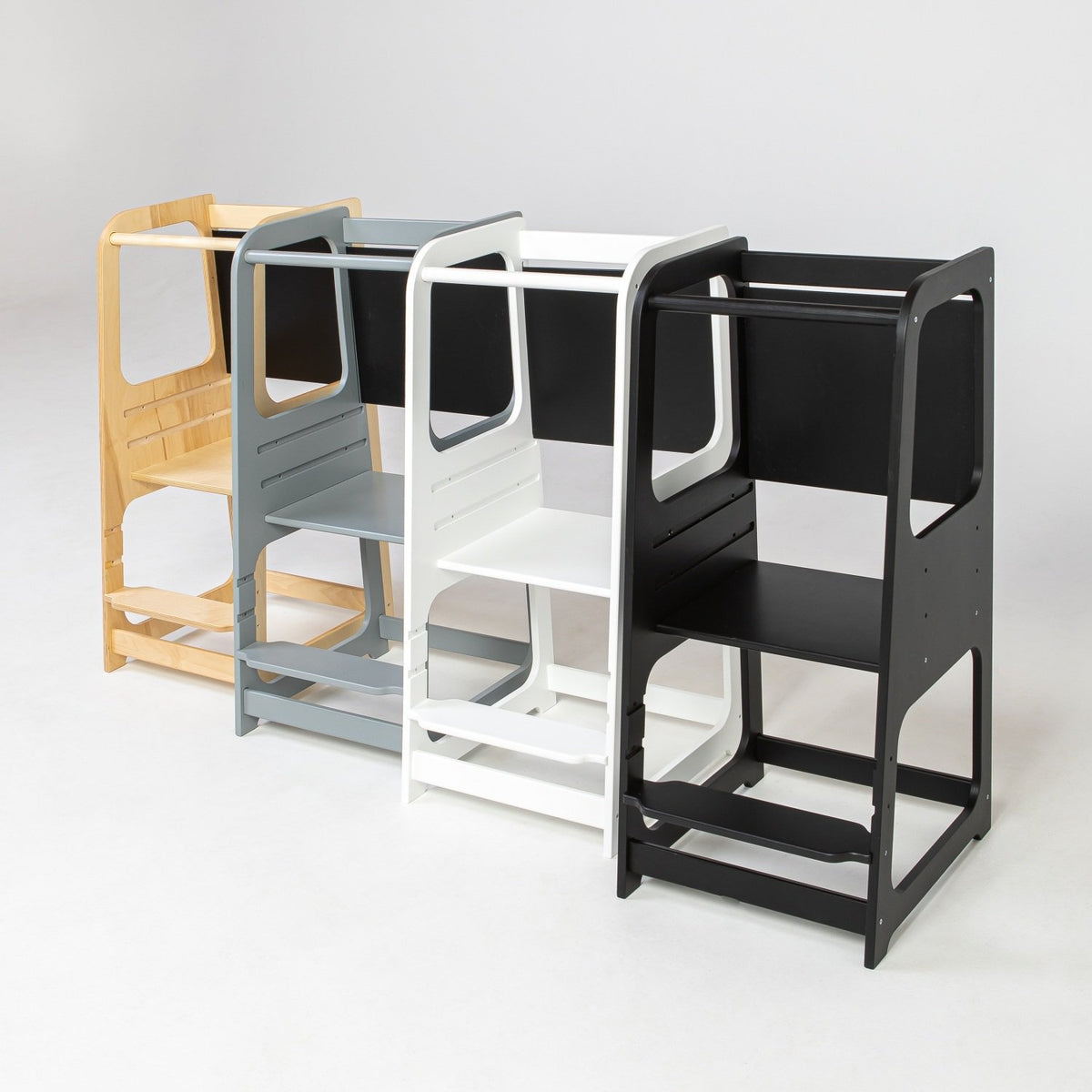 2. Lineup of Montessori kitchen helper towers in black, grey, white, and natural wood, shown in a studio setting