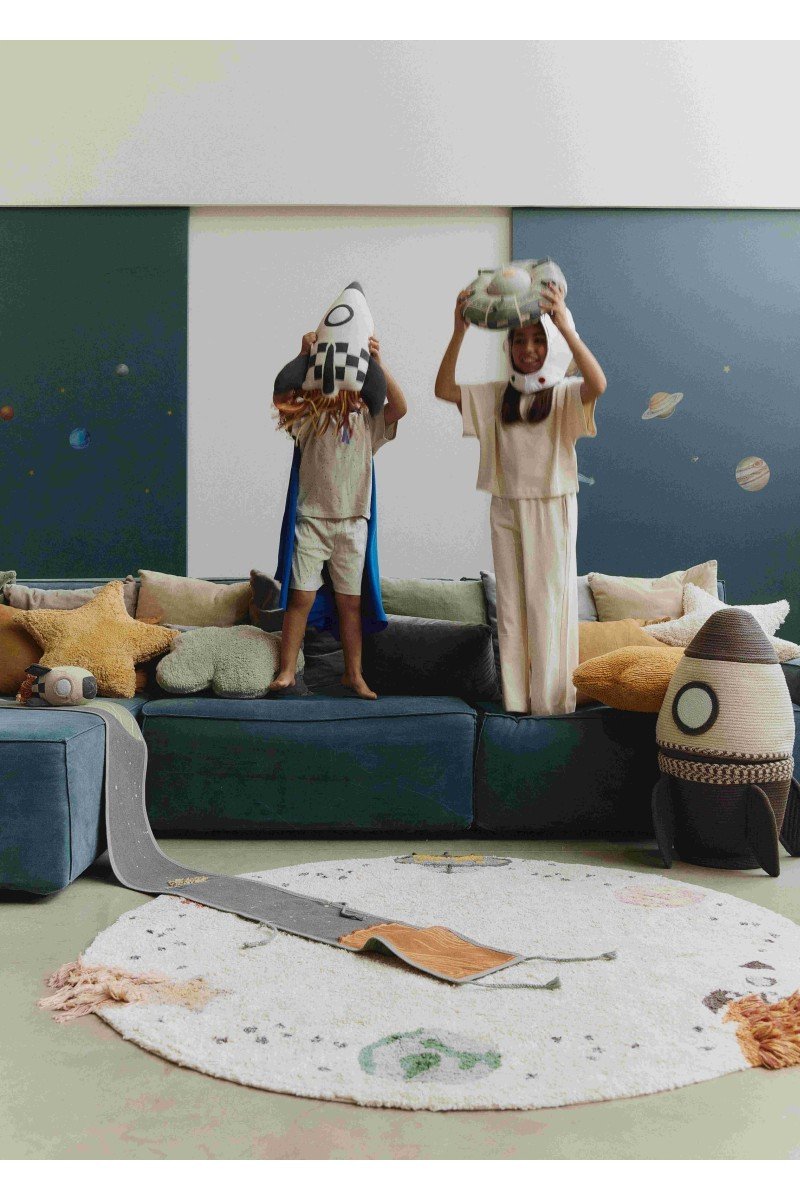 1. Two children playing with knitted rocket pillow in natural and dark gray with colorful fringes in a space-themed living room