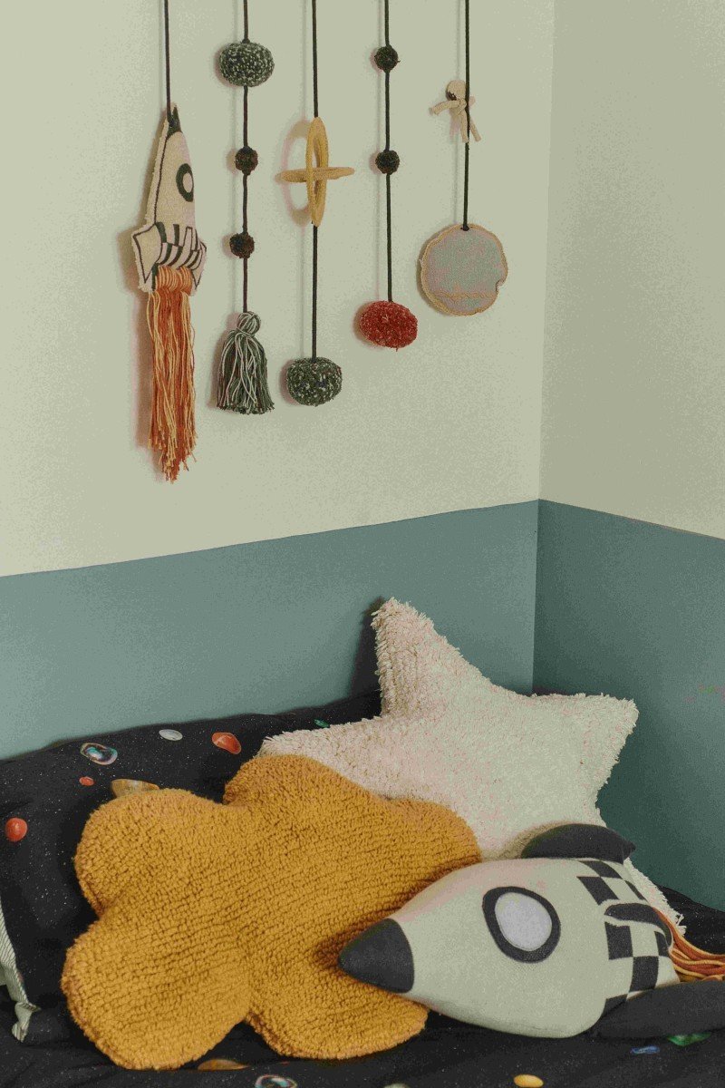 1. Knitted rocket pillow in natural and dark gray with colorful fringes on a bed with star-shaped cushions and wall decor