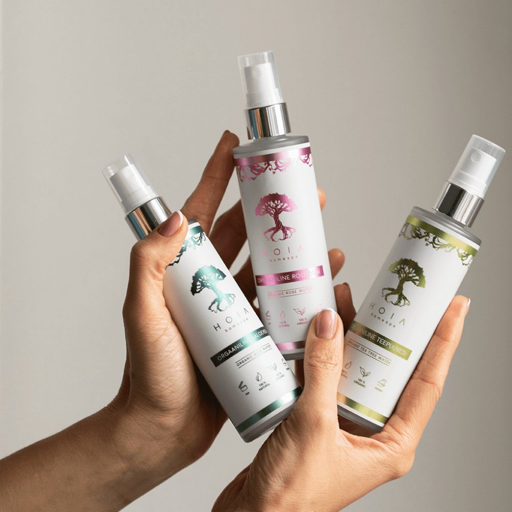 3. Hands holding HOIA homespa Organic Rose Water and other products in studio setting
