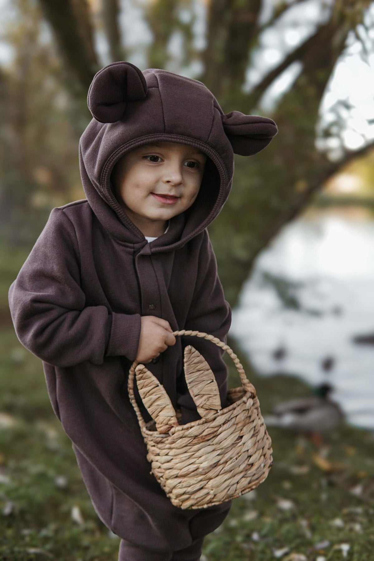 5. Child wearing chocolate brown eared jumpsuit with hood holding basket outdoors