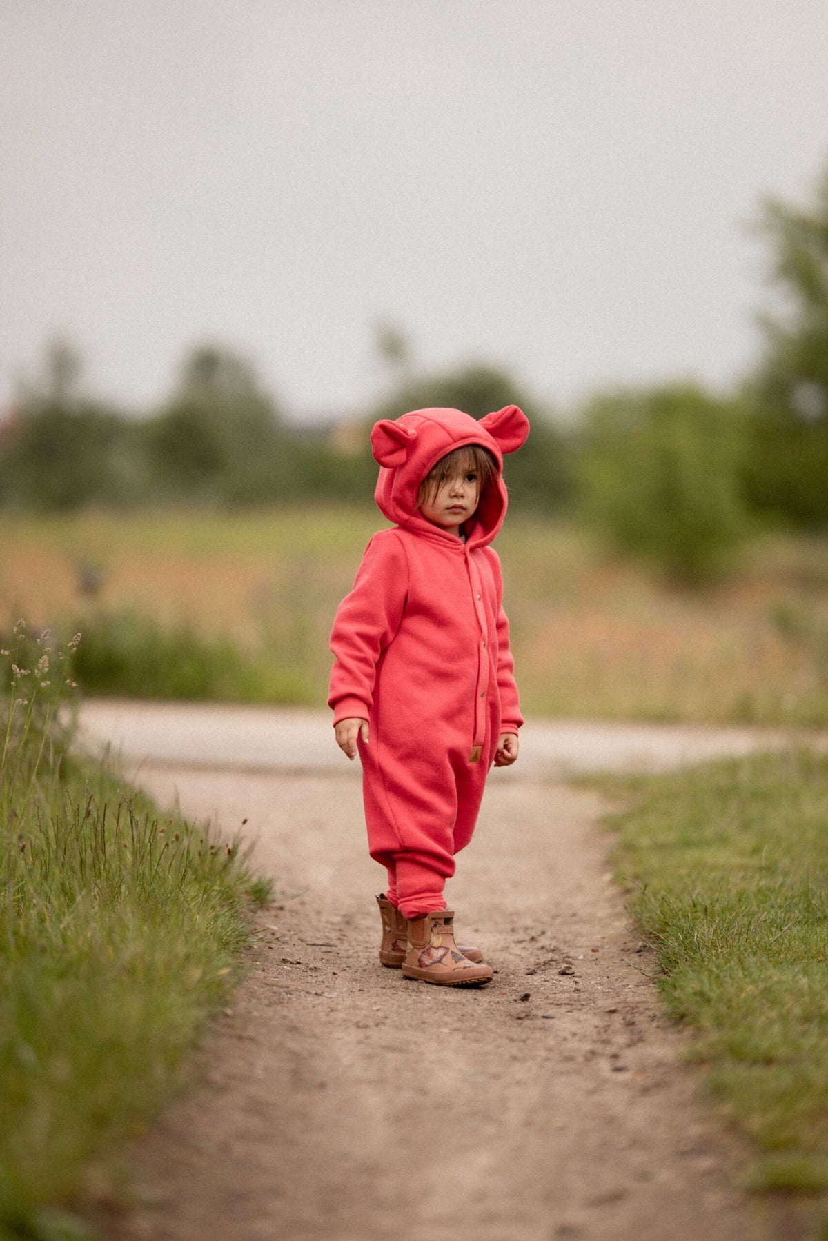 1. Child wearing coral eared jumpsuit by Zezuzulla standing on a path in a natural setting
