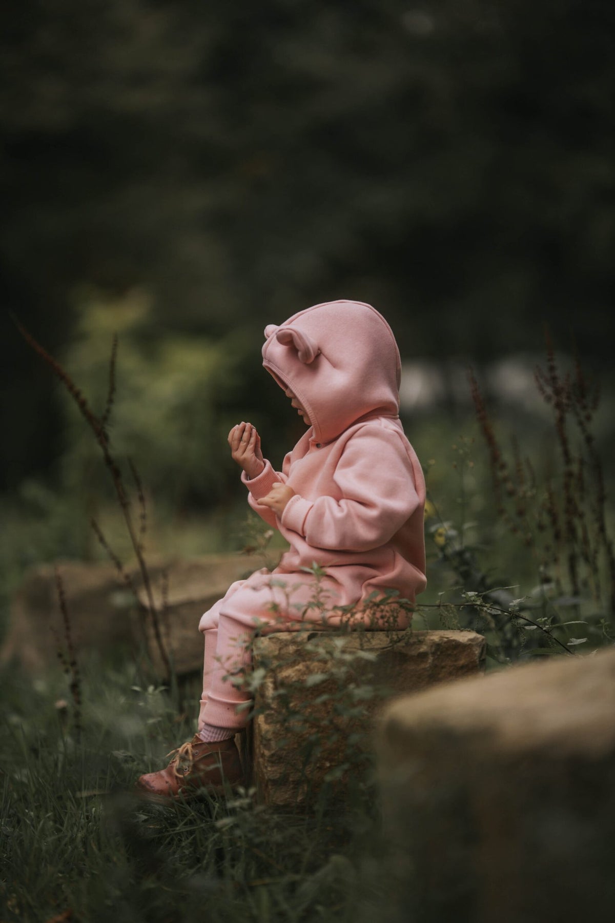 2. Child in peach eared jumpsuit sitting on a log, side view in a natural setting