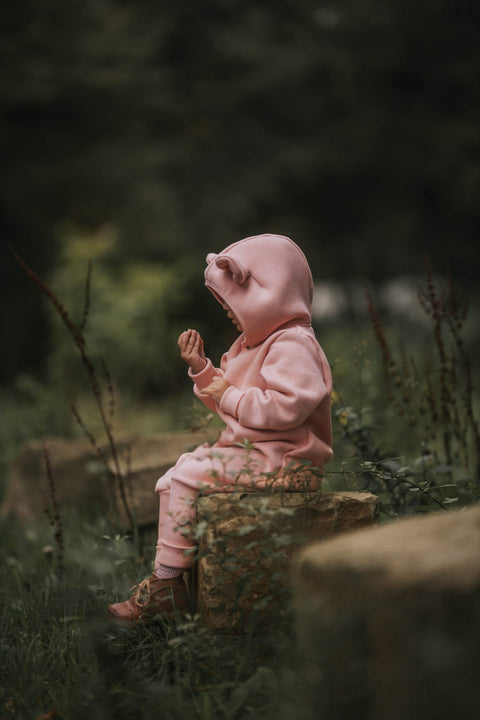 2. Child in peach eared jumpsuit sitting on a log, side view in a natural setting