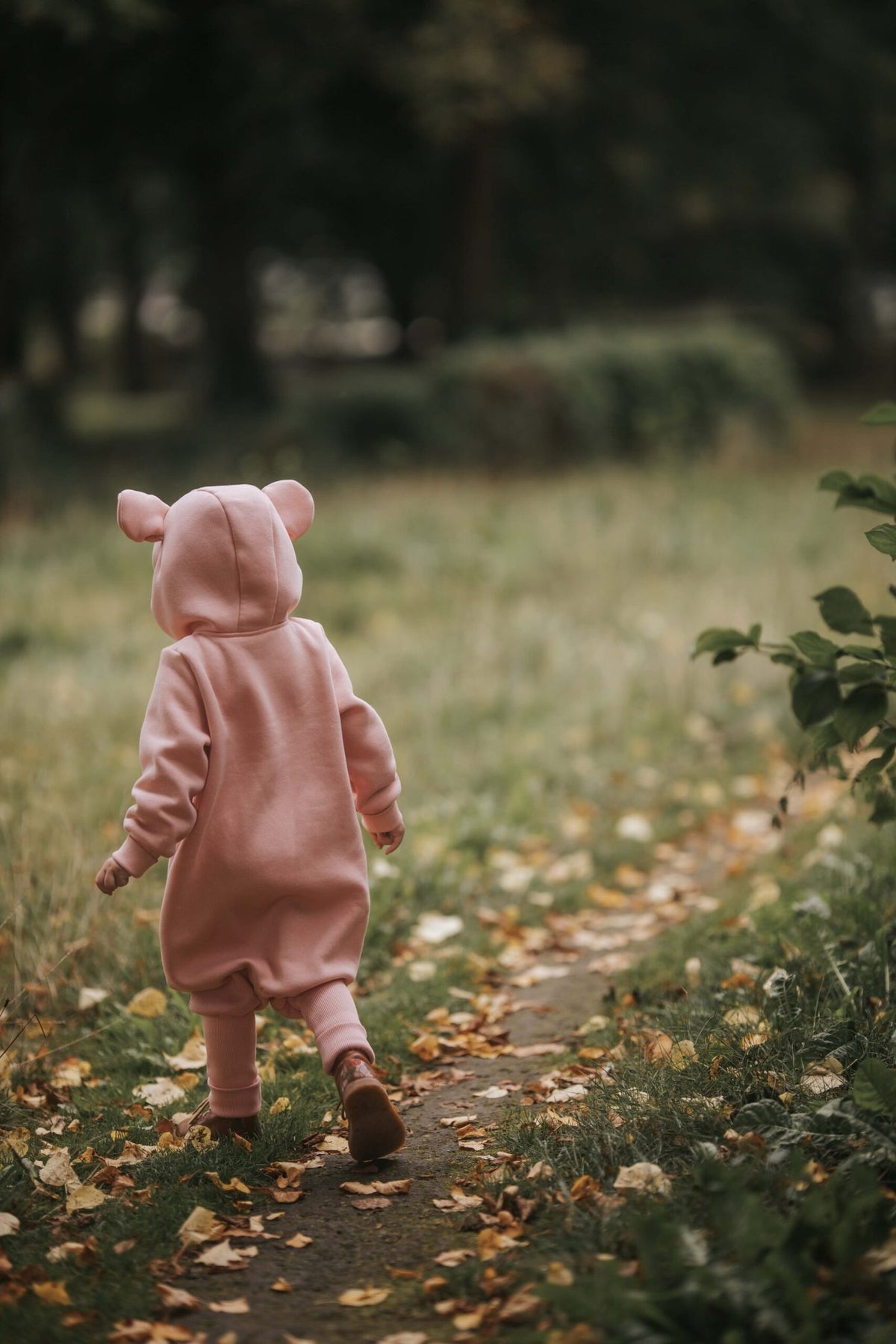 1. Child walking away in peach eared jumpsuit on a leaf-strewn path