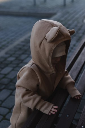 3. Close-up of baby in cacao eared jumpsuit with hood and ears, leaning on a bench
