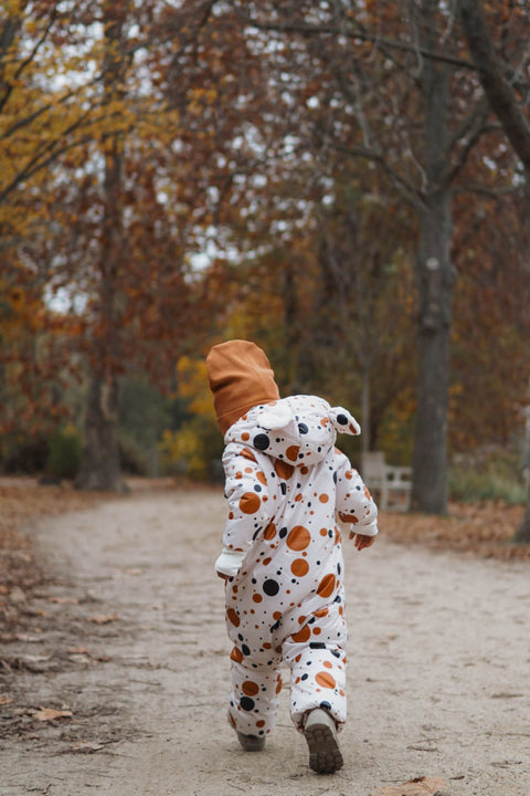 1. Child wearing black and orange polka dot winter jumpsuit with teddy bear ears, walking away on a forest path