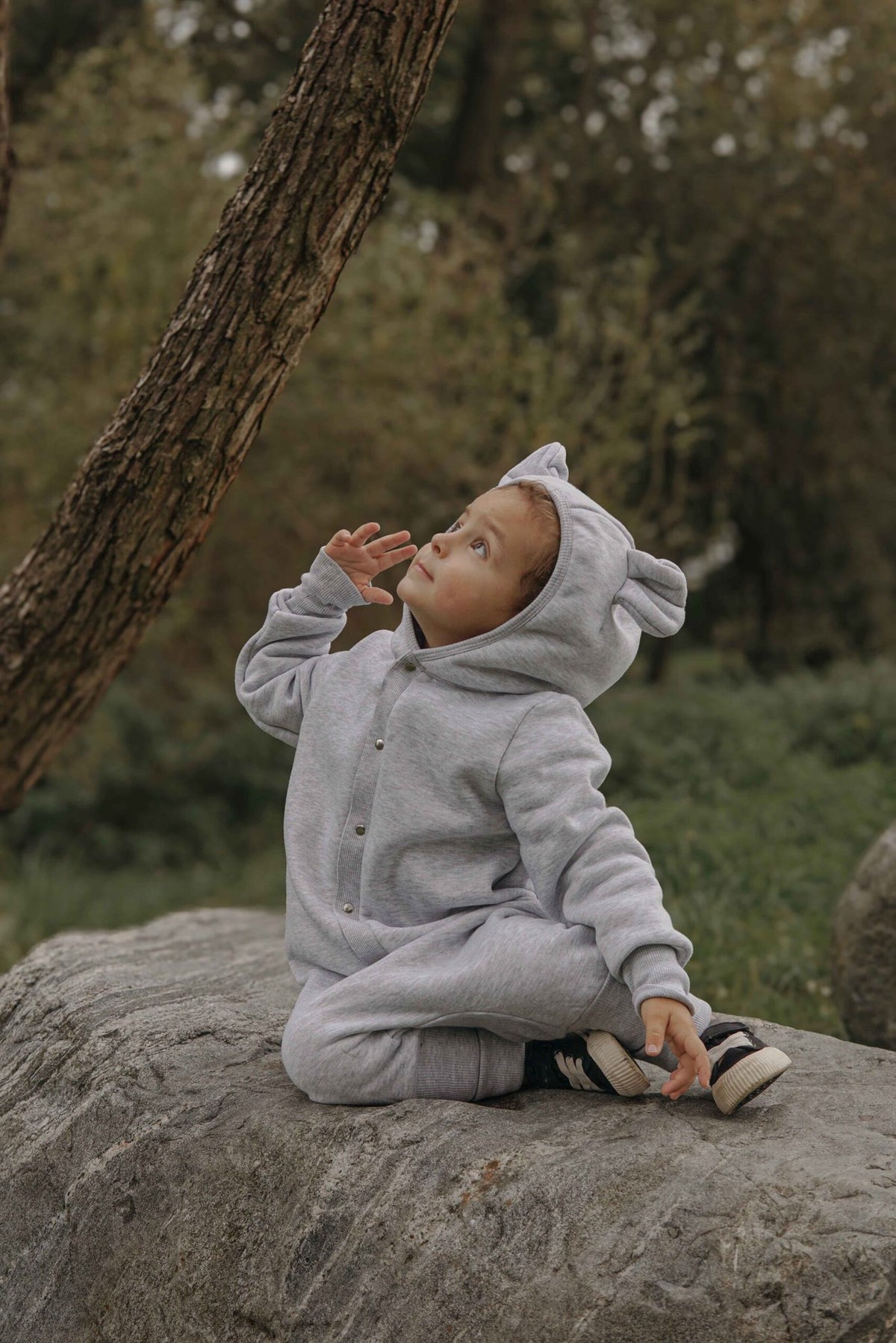 1. Child sitting on rock in park wearing Zezuzulla melange grey eared jumpsuit with hood