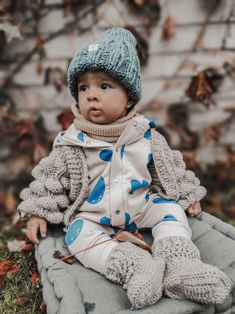 1. Baby wearing blue heart-patterned jumpsuit with hood and ears, sitting outdoors in autumn setting, paired with knitted hat and cardigan