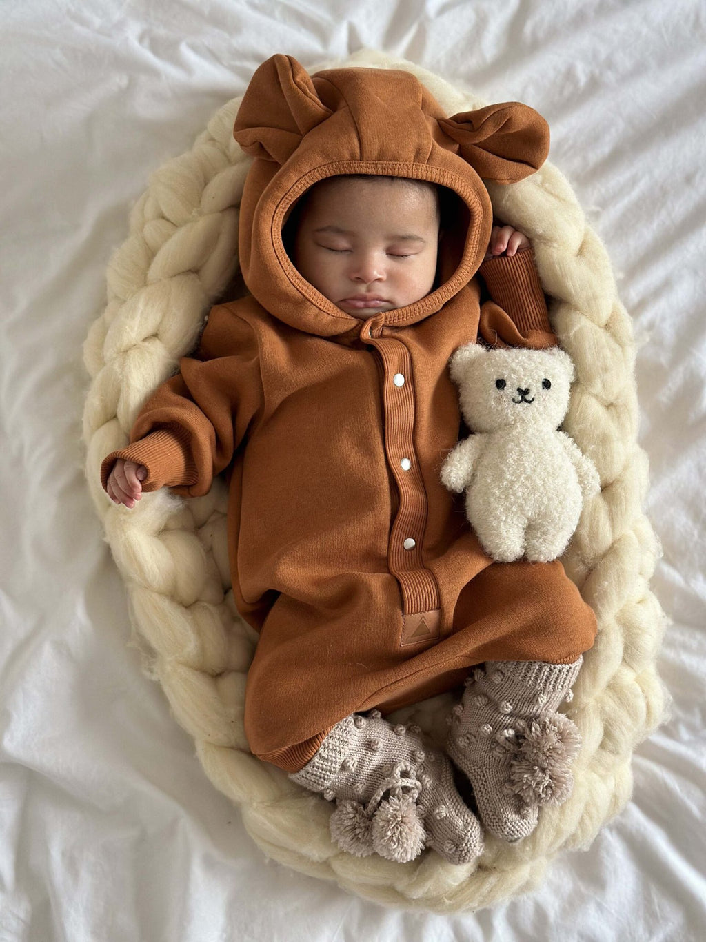 1. Sleeping baby in cinnamon eared jumpsuit with hood, holding teddy bear on knitted blanket
