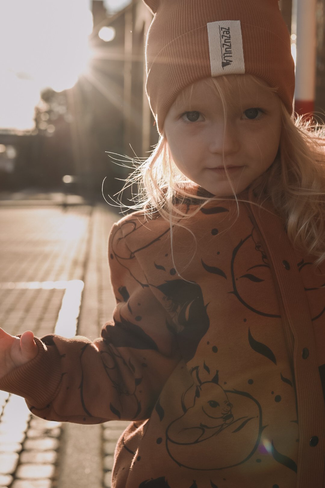 1. Girl in cinnamon squirrel jumpsuit with hood and ears, standing in sunlight on urban street