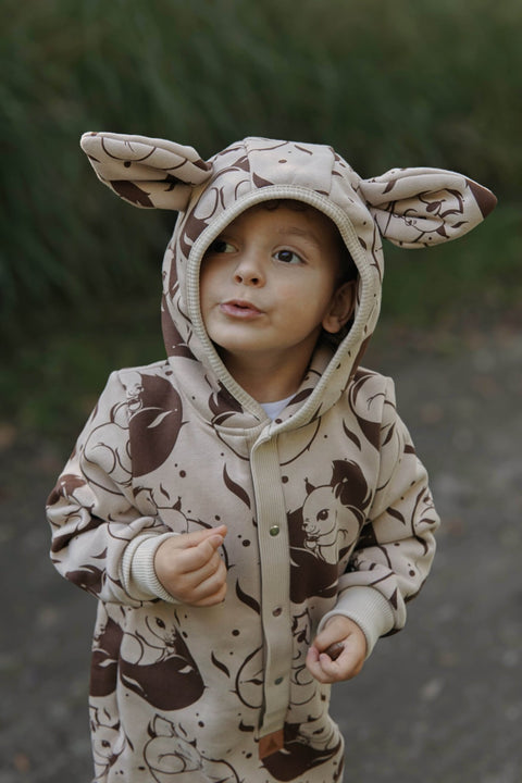 3. Close-up of child in beige squirrel print jumpsuit with hood and ears, outdoors