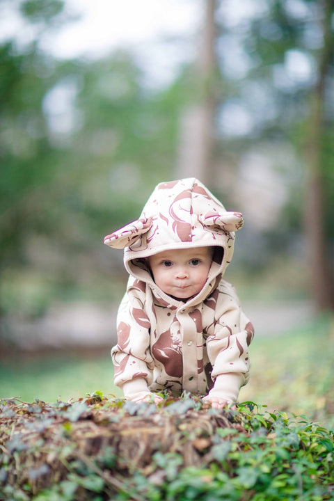 3. Baby crawling in beige squirrel print jumpsuit with hood and ears, outdoors on grass