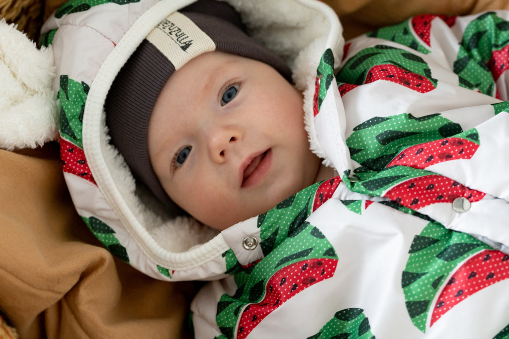 2. Close-up of baby in Zezuzulla watermelon print jumpsuit with teddy ears hood, lying on brown blanket
