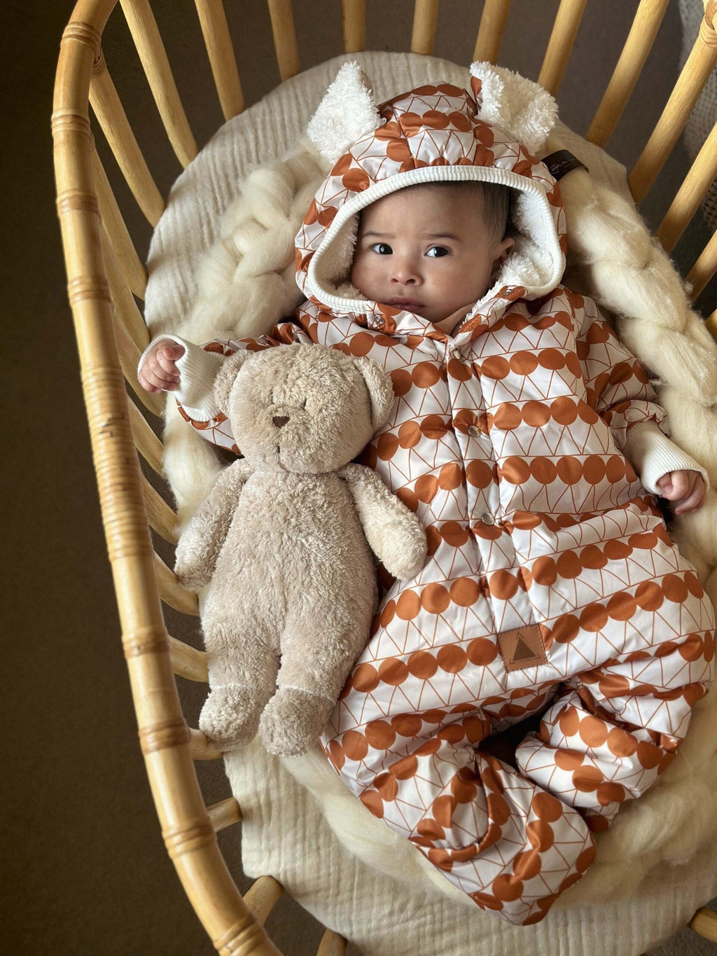 1. Baby in orange dotted jumpsuit with hood and bear ears, lying in a basket with a teddy bear