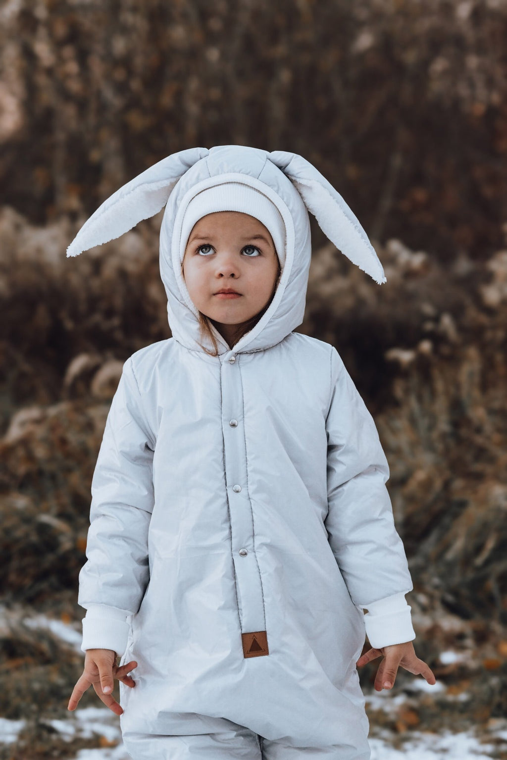 1. Child wearing Zezuzulla winter jumpsuit with rabbit ears in outdoor setting, showcasing waterproof polyester material and cozy design