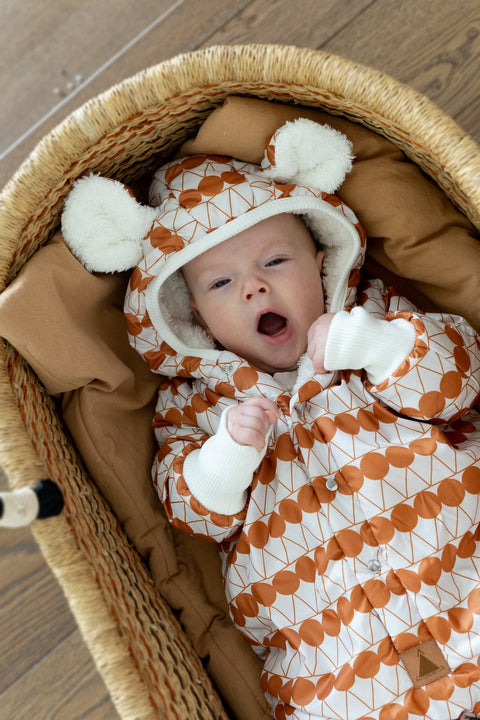 1. Baby yawning in orange dotted jumpsuit with hood and bear ears, lying in a woven basket