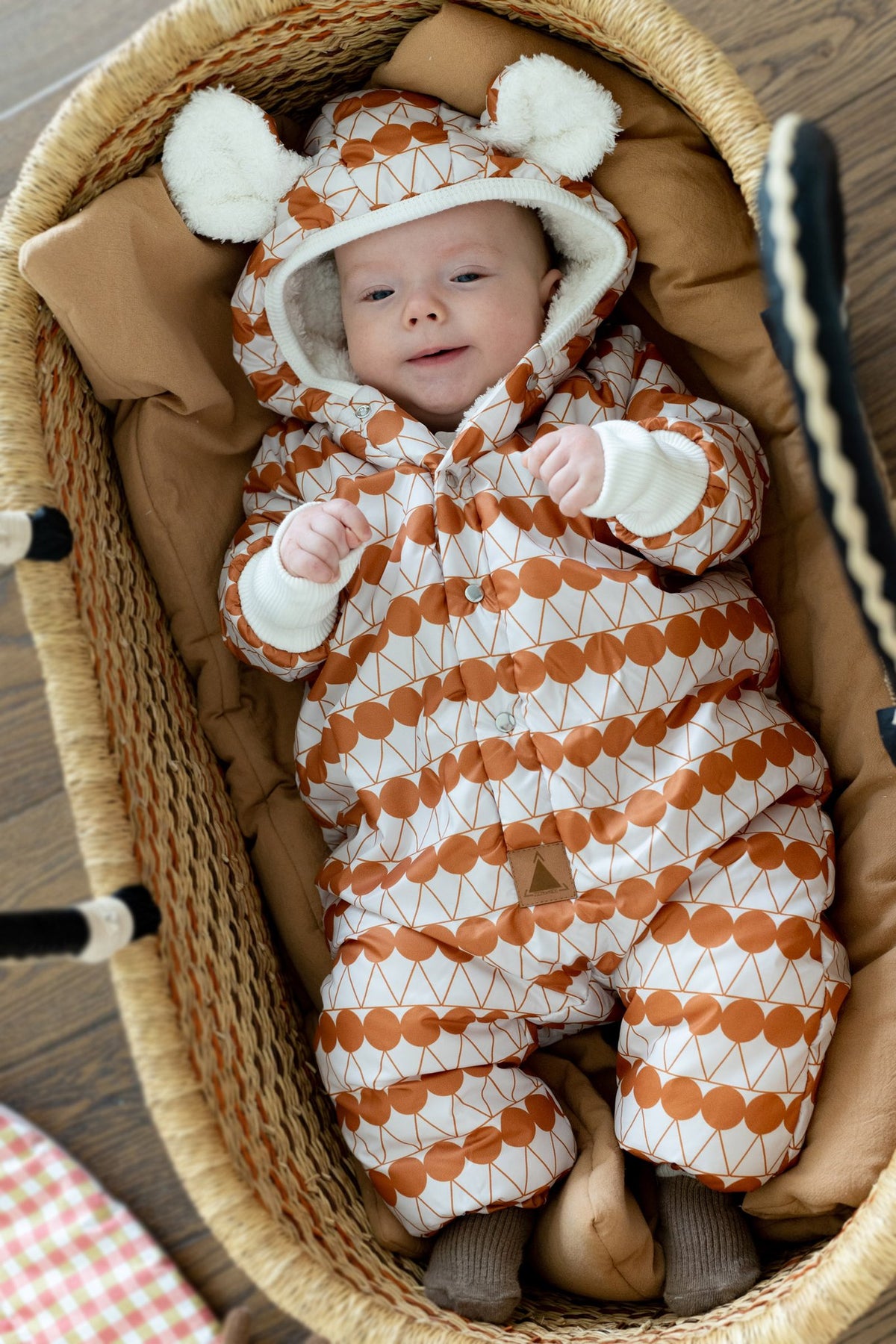 1. Smiling baby in orange dotted jumpsuit with hood and bear ears, lying in a woven basket